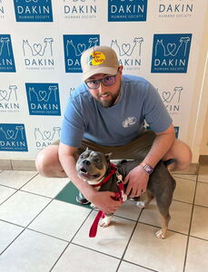 Man with baseball cap cradles dog he adopted at Dakin Humane Society