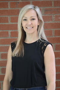 A woman in a black top standing in front of a brick wall