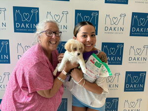 2 women hold a small white and tan puppy they adopted at Dakin's adoption event